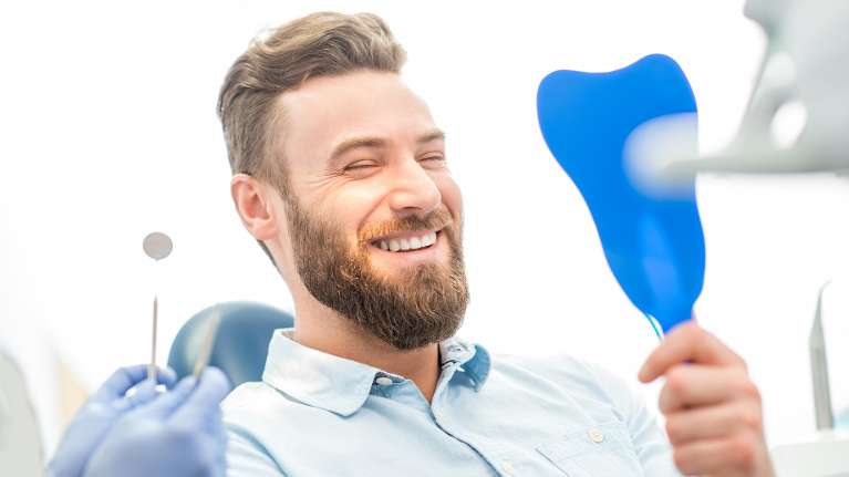 Man looking at himself in the mirror after getting porcelain veneers from Cook Family Dental